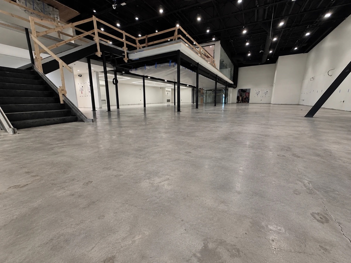 Bare polished concrete floor in a large commercial retail space under construction, with a black staircase and mezzanine